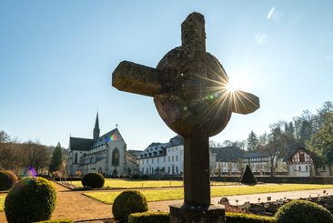 Sonnenstrahlen hinter einem Kreuz in einer ruhigen Landschaft