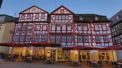 Äußeres eines historischen Hauses mit roten Sonnenschirmen und Tischen