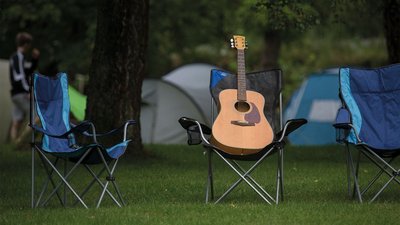 Gitarre steht auf einem Campingstuhl, Zelt im Hintergrund