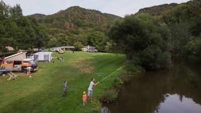 Ein Campingplatz mit Angler, Kindern und Wohnmobilen in der Natur