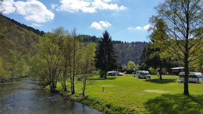 Sicht auf einen Campingplatz am Fluss mit Bäumen und Berglandschaft