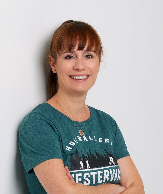 Frau mit langen Haaren steht an einer weißen Wand und lächelt.