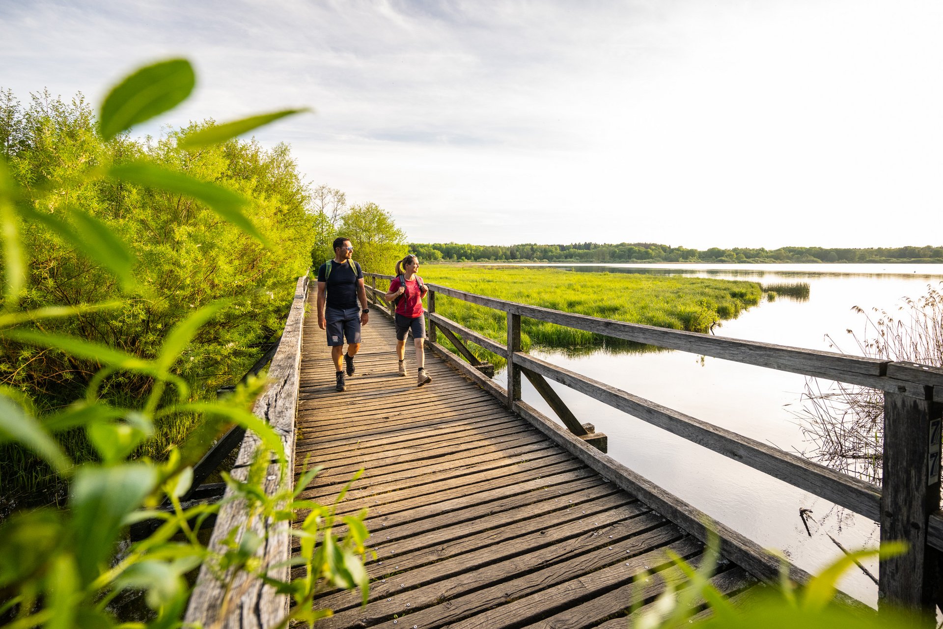 Paar, das eine Holzbrücke entlang eines Gewässers bei Sonnenlicht geht.