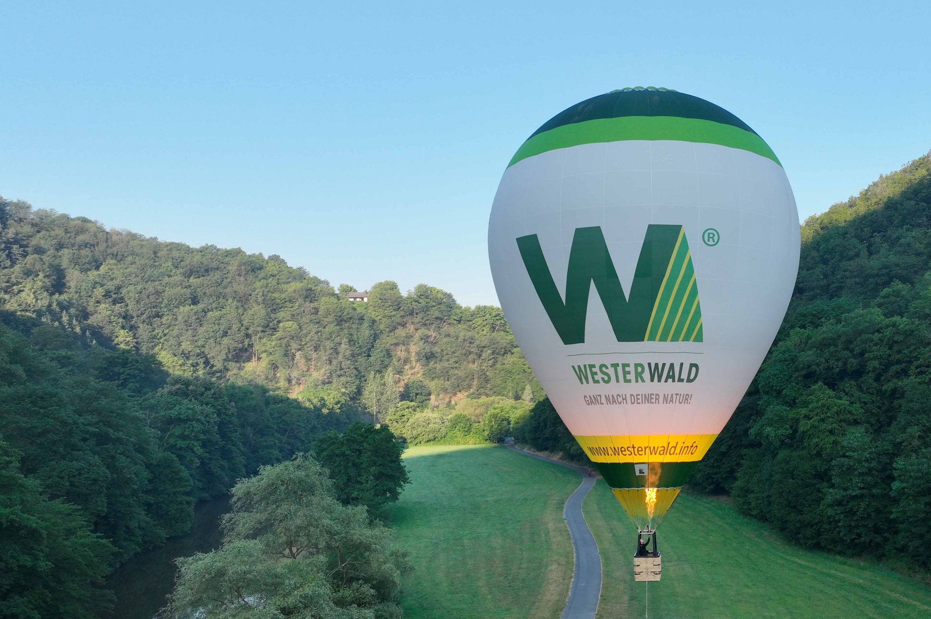 Farbiger Heißluftballon schwebt über eine grüne Landschaft im Westerwald