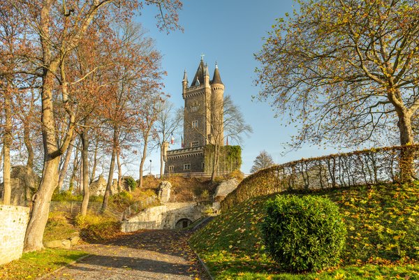 Malerei eines Schlosses umgeben von Bäumen und herbstlichen Farben