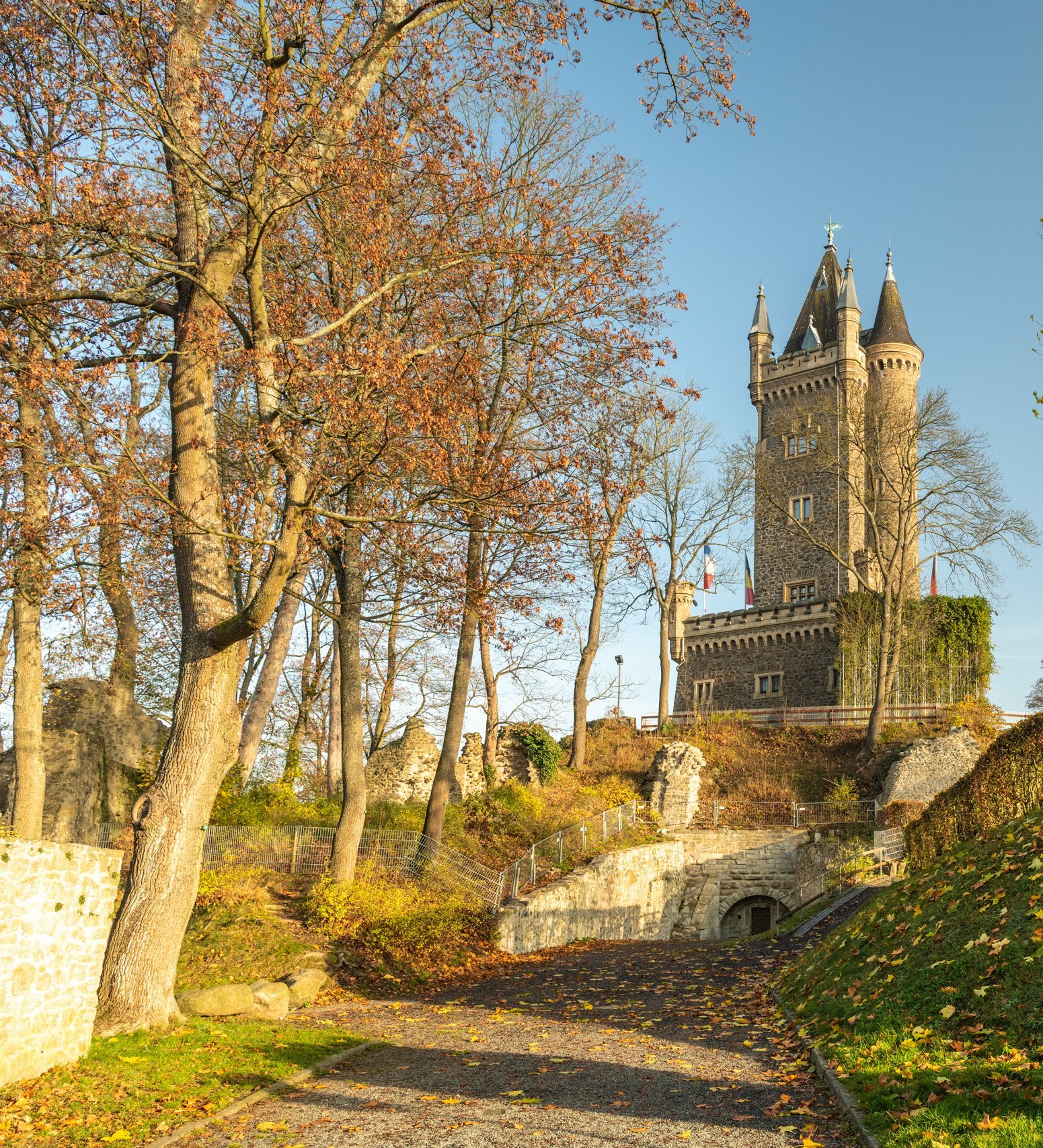 Malerei eines Schlosses umgeben von Bäumen und herbstlichen Farben