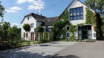 Helles, grünes Haus mit Bepflanzung und Parkplatz