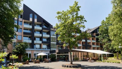Heller Gebäudekomplex mit Bäumen und Sitzbereichen im Freien