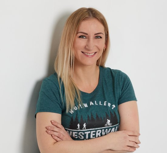 Frau in T-Shirt mit Naturmotiven steht lächelnd vor einer Wand