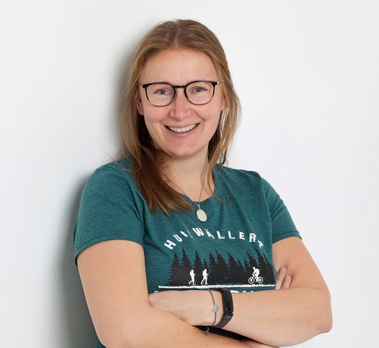 Person mit Brille und sportlichem T-Shirt steht lächelnd an einer Wand