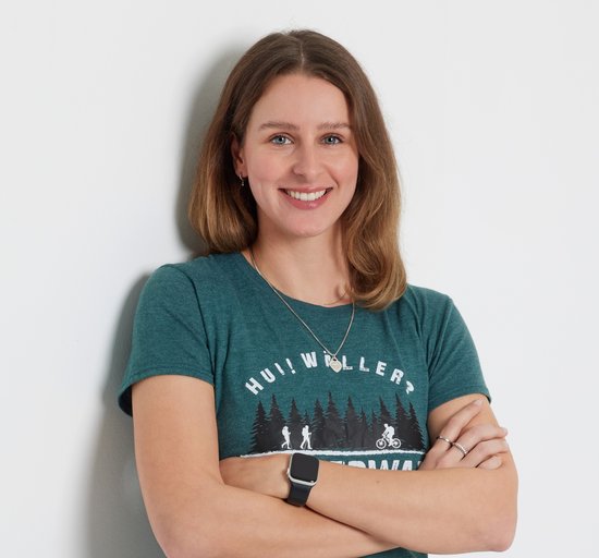Eine Frau mit T-Shirt steht lächelnd vor einer weißen Wand.