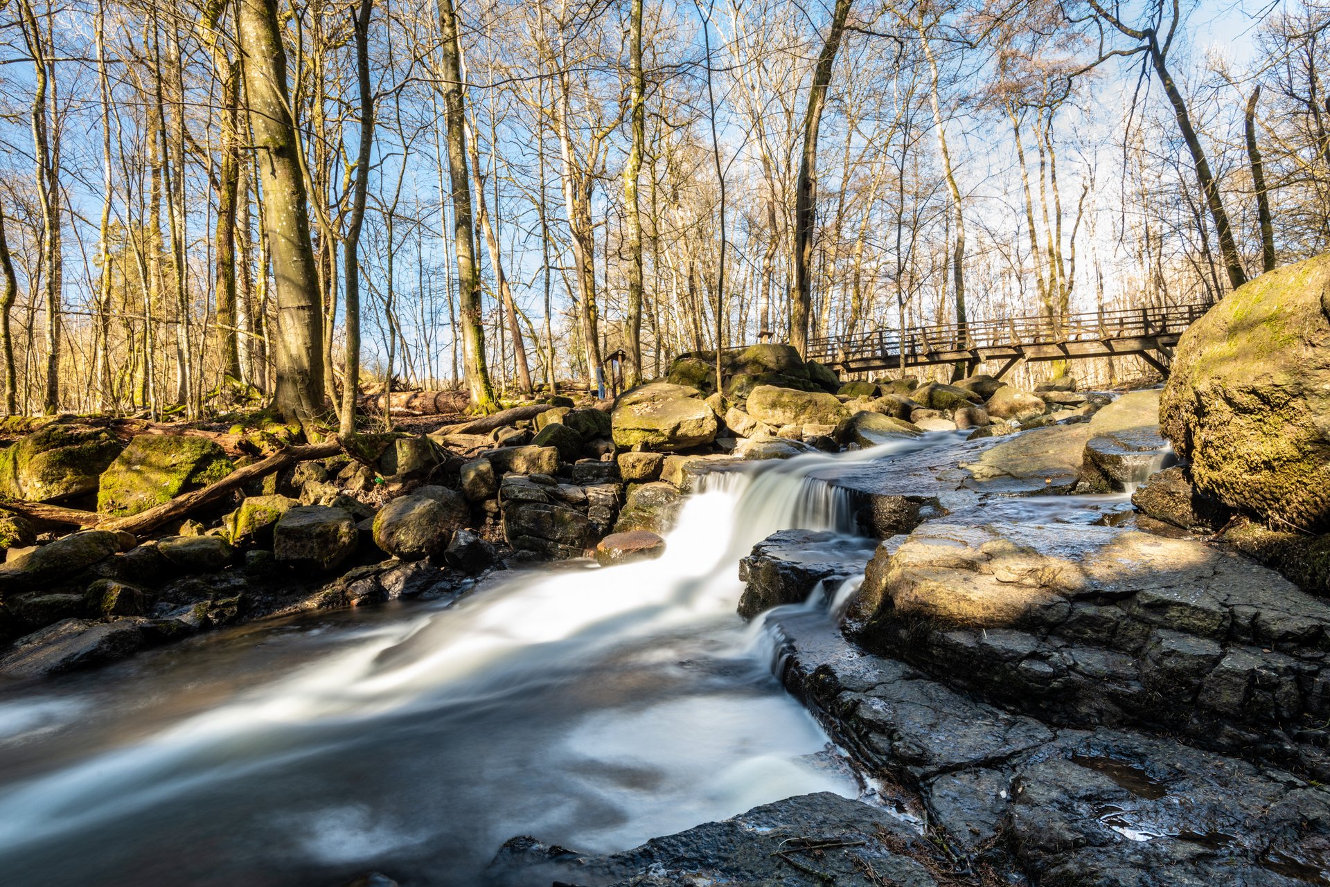 Sanfter Wasserlauf zwischen Steinen im Wald mit Brücke