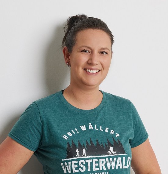 Frau posiert lächelnd an einer Wand in einem grünen T-Shirt
