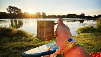 Person holding a cup by the water during sunset