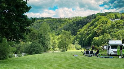 Weite Wiese mit Campingausstattung und bewaldeter Landschaft