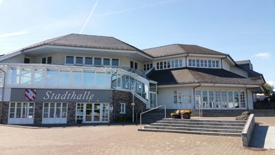 Ansicht der Stadthalle mit großen Fenstern und Treppe bei klarem Himmel