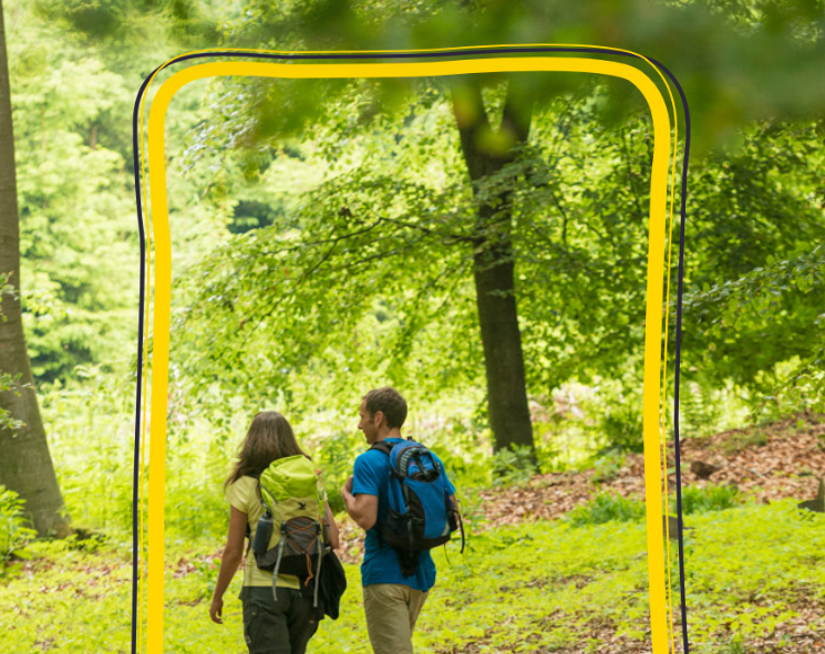 Zwei Wanderer gehen durch einen Wald mit einem gelben Rahmen
