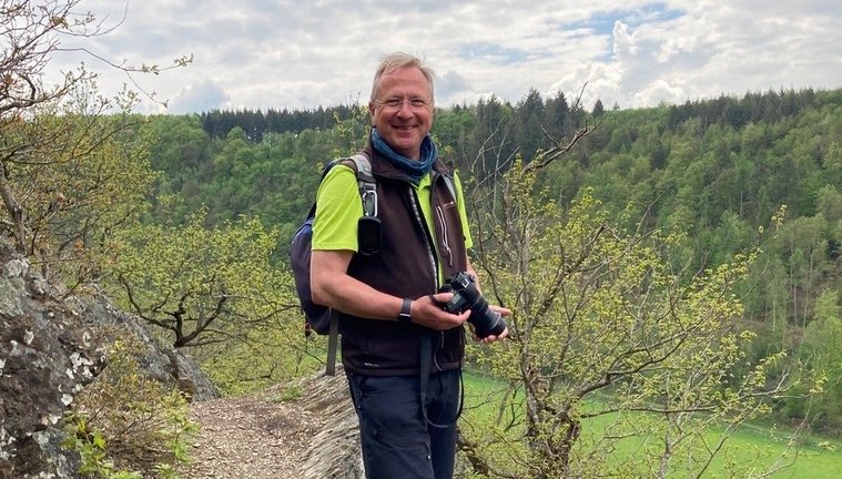 Ein Wanderführer steht auf einem Weg mit Kamera in der Hand