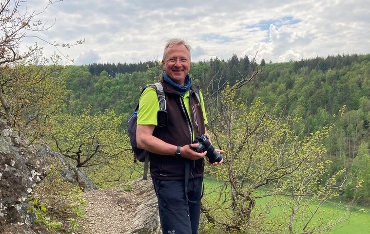 Ein Wanderführer steht auf einem Weg mit Kamera in der Hand