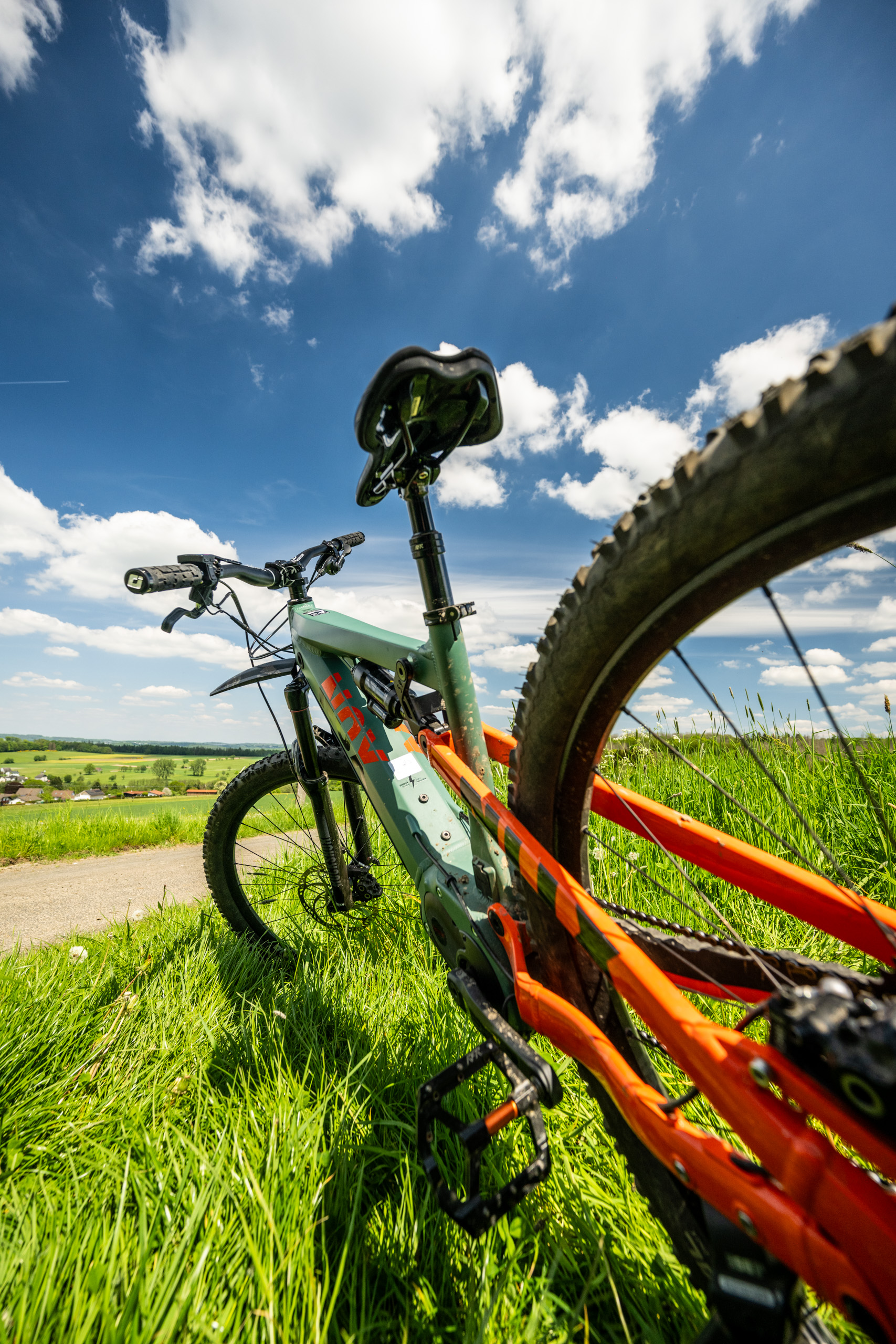 Fahrrad im Vordergrund, umgeben von Gras und Wolken