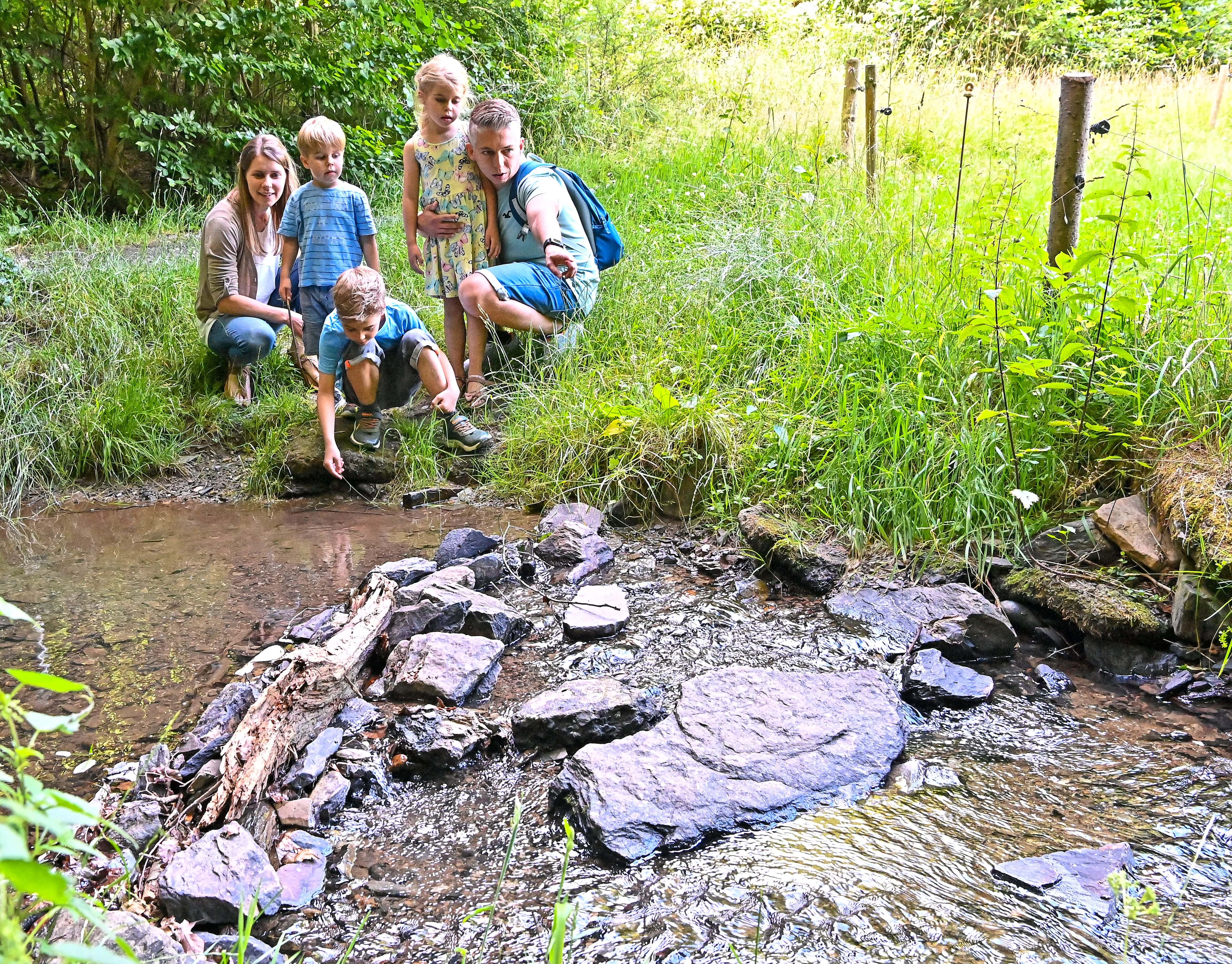 Eine Familie steht am Bachrand und beobachtet das Wasser.