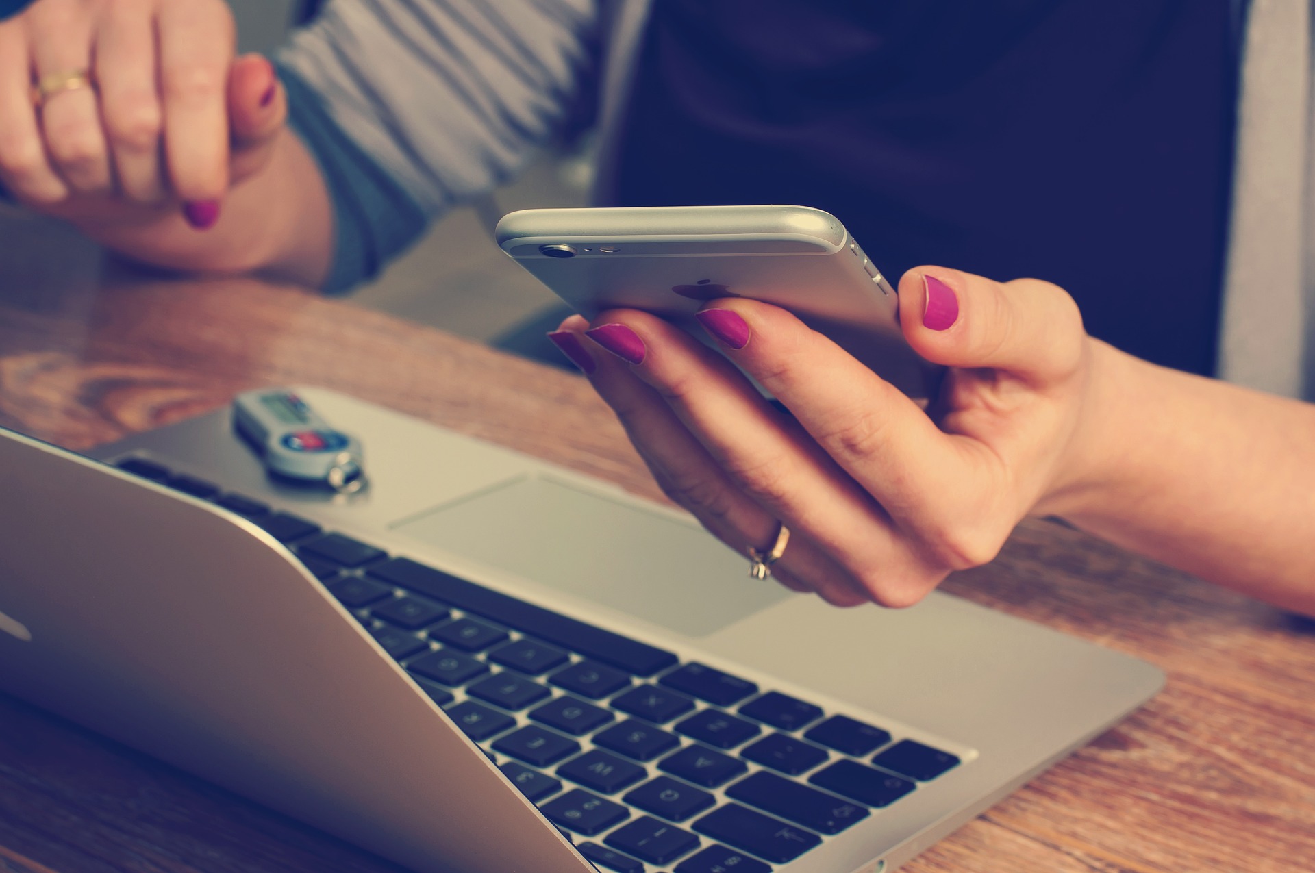 Hände einer Person, die ein Smartphone neben einem Laptop benutzt