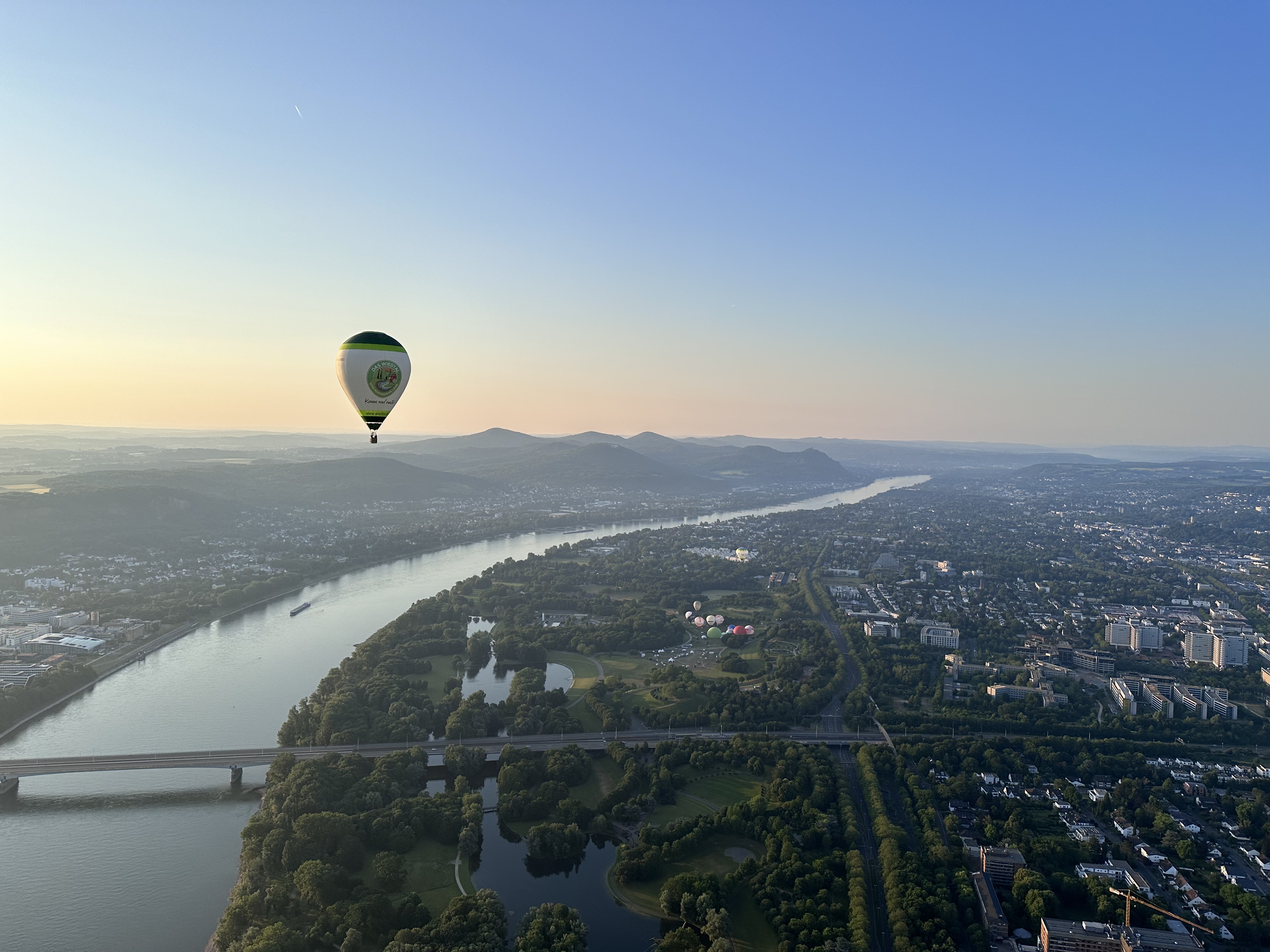 Heißluftballon schwebt über einer Landschaft mit Fluss und Bergen