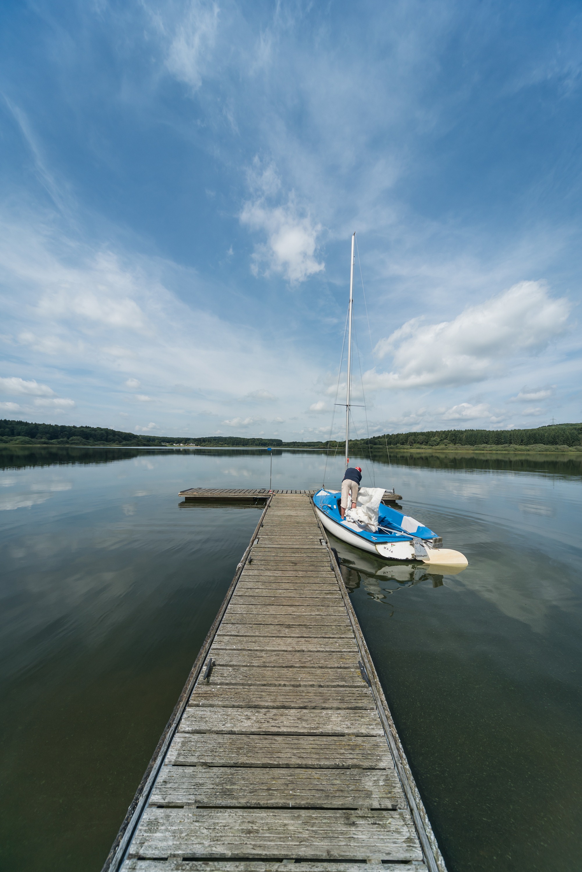 Ein Steg führt zu einem Ruderboot in einem stillen See unter blauem Himmel