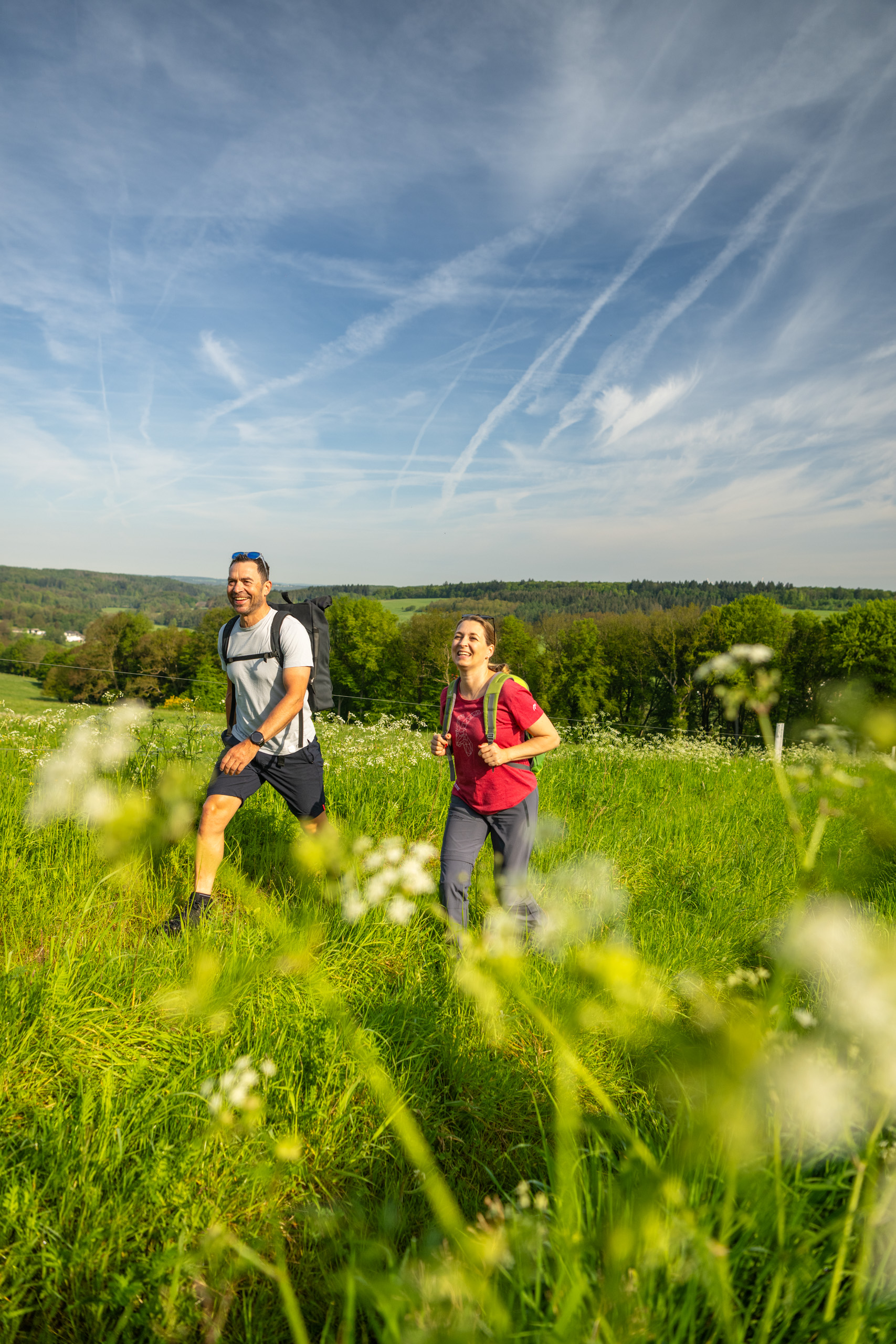 Zwei Personen wandern durch eine grüne Landschaft unter blauem Himmel