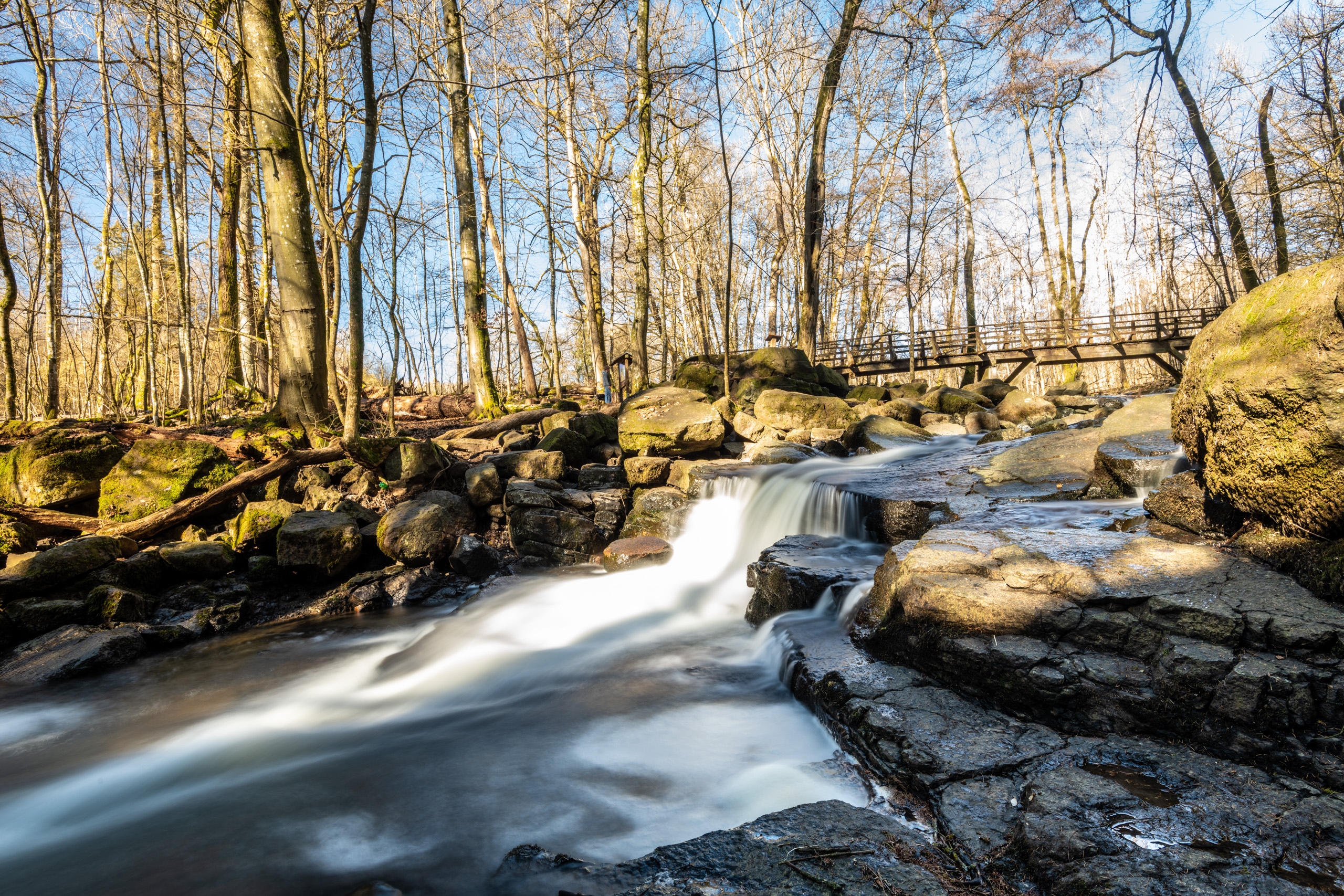 Sanfter Wasserlauf zwischen Steinen im Wald mit Brücke
