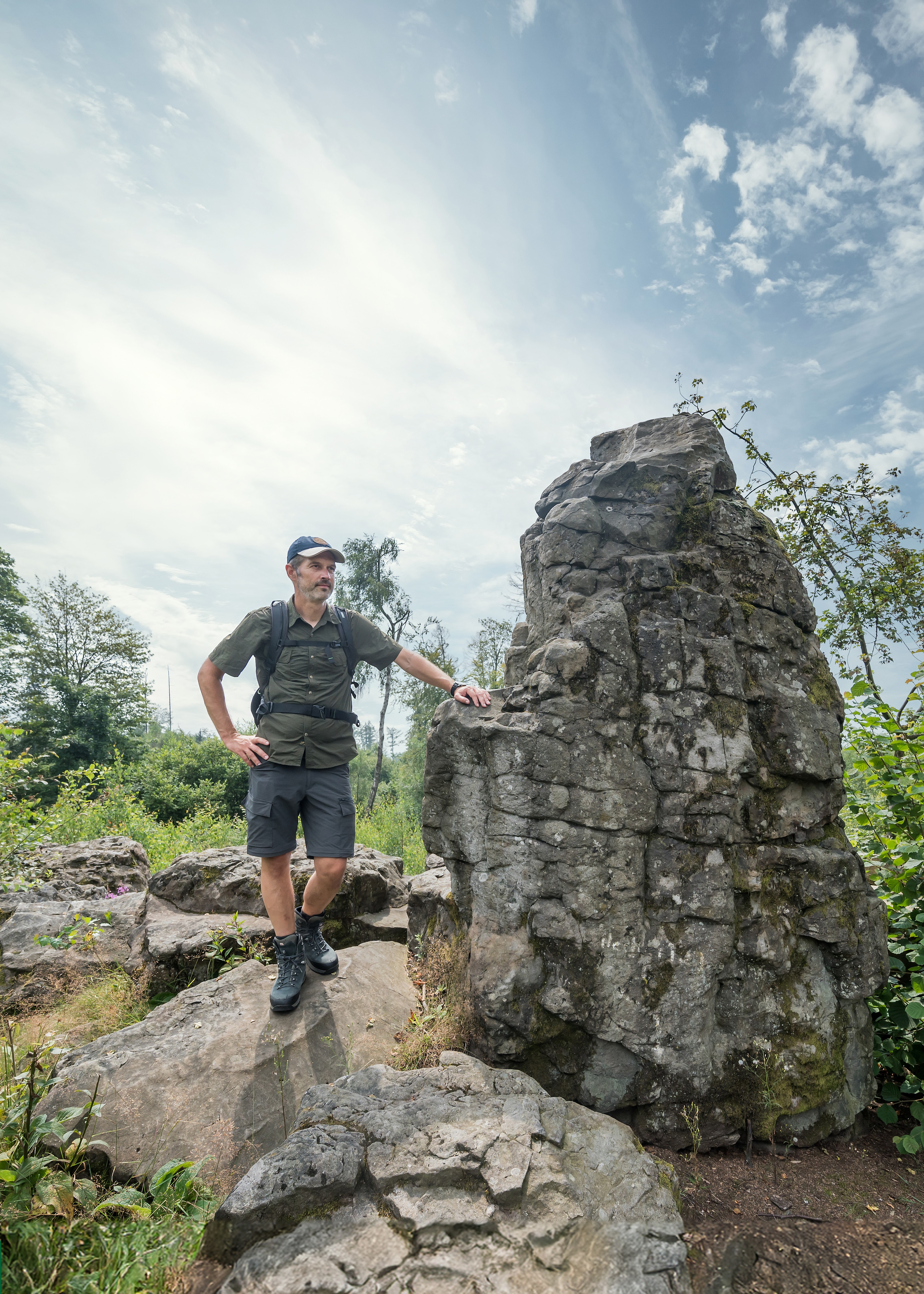 Mann steht an einem großen Felsen unterhalb eines bewölkten Himmels